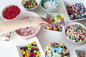 kid-reaching-for-colorful-candy-in-bowls-on-a-white-table-1024x682
