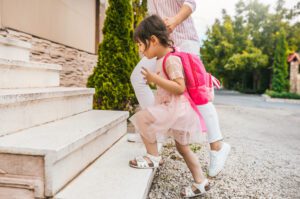 Image of mother and pupil daughter going back at home from kindergarten. Good relationship. Happy cute little girl with her mom feel happy after the preschool day, climb up the stairs at home outside